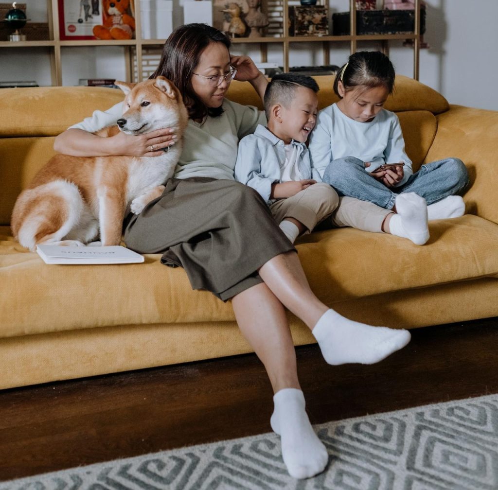A mother relaxing on a couch with her two children and their pet dog.