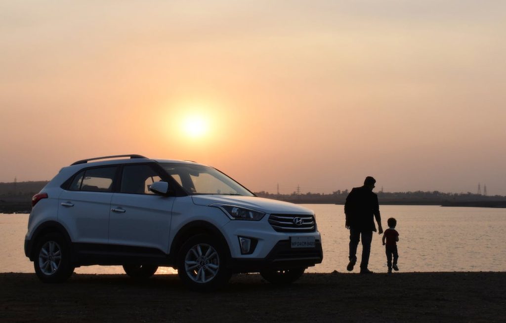 An SUV at the river's edge, a man and a child silhouetted by the sun.